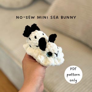 Könnte beinhalten: Ein handgehäkeltes Seehasen-Amigurumi in Weiß mit schwarzen Akzenten und türkisfarbenen Augen. Der Text "NO-SEW MINI SEA BUNNY" steht über dem Häschen. Ein weißer Kreis mit dem Text "PDF pattern only" befindet sich unten rechts.