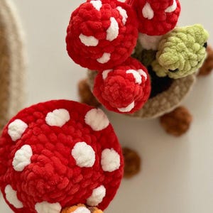 May include: Crocheted mushroom and turtle toys. The mushrooms are red with white spots. The turtle has a green head and brown shell. The toys are made of soft, textured yarn.
