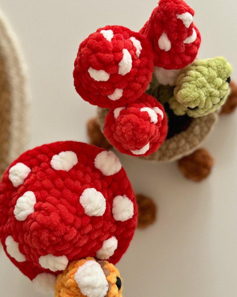 May include: Crocheted mushroom and turtle toys. The mushrooms are red with white spots. The turtle has a green head and brown shell. The toys are made of soft, textured yarn.