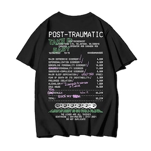 May include: A black short-sleeve t-shirt featuring a white graphic print resembling a store receipt. The text includes 'POST-TRAUMATIC', a list of disorders with prices, and handwritten-style notes in purple and green ink across the back.