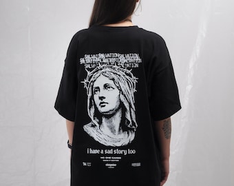 May include: A black short-sleeve t-shirt featuring a white graphic print on the back. The design displays a portrait of a figure wearing a crown of thorns, the repeated word SALVATION, and the text i have a sad story too NO ONE CARES.
