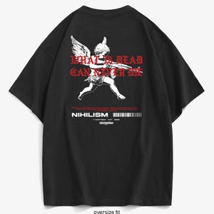 Peut inclure: T-shirt noir oversize avec un motif blanc d'un ange tenant une arme à feu et le texte rouge "WHAT IS DEAD CAN NEVER DIE". Le t-shirt comporte également le mot "NIHILISM" et un code-barres.