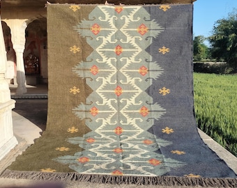 May include: A handwoven rug with a geometric pattern in shades of blue, green, and orange. The rug has a fringe border and is made of wool.