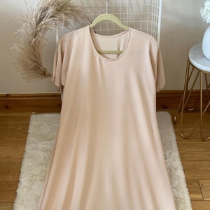 May include: A long, loose-fitting, light beige maxi dress with short sleeves and a round neckline.