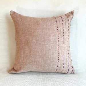 Puede incluir: Una almohada de sofá marrón con una banda decorativa cosida en rojo y dorado.