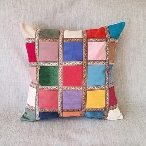 May include: A colorful square patterned throw pillow with gold trim. The pillow is made of velvet and has a variety of colors including red, blue, green, yellow, and purple.
