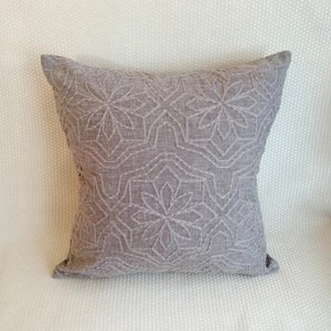 Puede incluir: Una almohada gris con un diseño floral bordado. La almohada está hecha de una tela suave y texturizada.