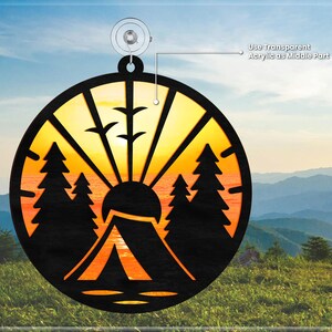 May include: A round wooden ornament with a sunset scene, a tent, and trees. The ornament is designed to be layered with a transparent acrylic piece in the center.