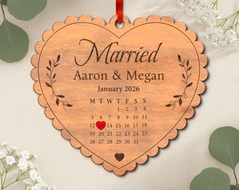 May include: Wooden heart-shaped ornament with scalloped edges and a red ribbon. The ornament is engraved with the word "Married", names, and the date January 2026. A calendar highlights the 14th day of the month with a heart.