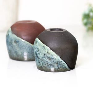 Pu&ograve; includere: Due vasi in ceramica dal design unico. La met&agrave; superiore di ogni vaso &egrave; di colore marrone scuro, mentre la met&agrave; inferiore &egrave; blu teal con una finitura strutturata e smaltata. I vasi hanno una forma arrotondata e una piccola apertura nella parte superiore.