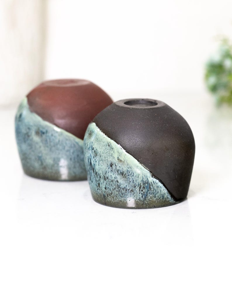 Pu&ograve; includere: Due vasi in ceramica dal design unico. La met&agrave; superiore di ogni vaso &egrave; di colore marrone scuro, mentre la met&agrave; inferiore &egrave; blu teal con una finitura strutturata e smaltata. I vasi hanno una forma arrotondata e una piccola apertura nella parte superiore.
