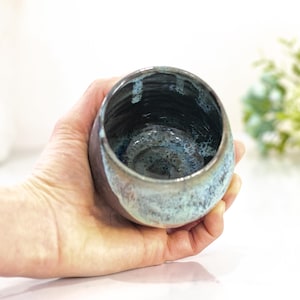 Pu&ograve; includere: Una ciotola in ceramica fatta a mano con interno scuro ed esterno azzurro e marrone. La ciotola &egrave; tenuta in mano, mostrando la sua smaltatura e forma uniche. La ciotola &egrave; un pezzo decorativo.