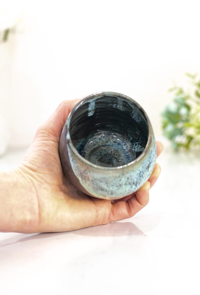 Pu&ograve; includere: Una ciotola in ceramica fatta a mano con interno scuro ed esterno azzurro e marrone. La ciotola &egrave; tenuta in mano, mostrando la sua smaltatura e forma uniche. La ciotola &egrave; un pezzo decorativo.