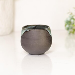 Pu&ograve; includere: Una tazza in ceramica grigio scuro fatta a mano, con una base arrotondata e un bordo leggermente svasato. Il bordo presenta una glassa turchese a contrasto. Questa tazza unica e moderna &egrave; perfetta per caff&egrave; o t&egrave;.