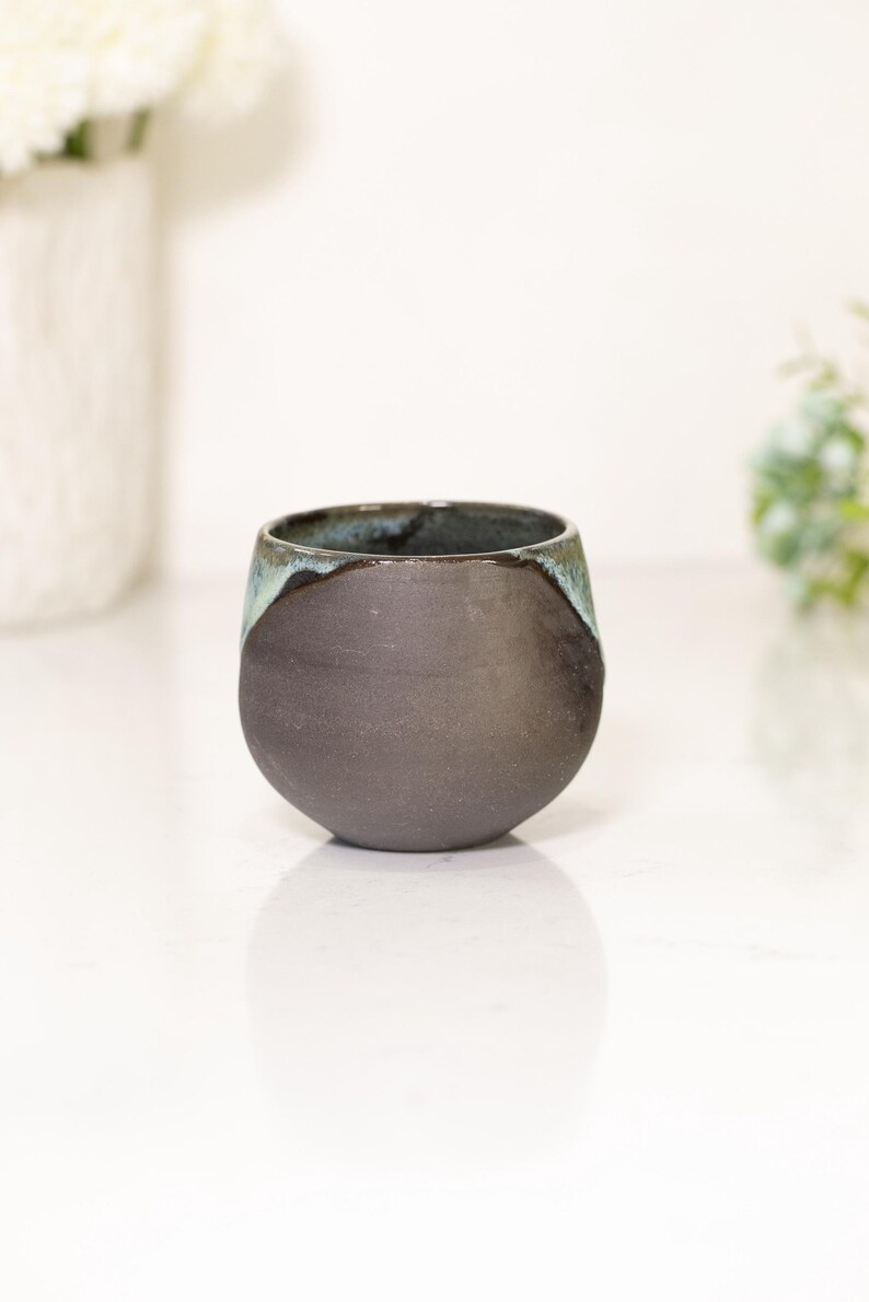 Pu&ograve; includere: Una tazza in ceramica grigio scuro fatta a mano, con una base arrotondata e un bordo leggermente svasato. Il bordo presenta una glassa turchese a contrasto. Questa tazza unica e moderna &egrave; perfetta per caff&egrave; o t&egrave;.