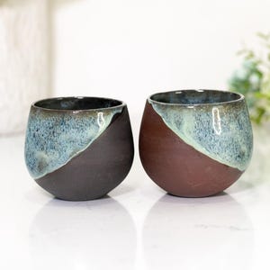 Pu&ograve; includere: Due bicchieri da vino senza stelo in ceramica fatti a mano. Uno &egrave; marrone scuro e blu, l'altro &egrave; marrone e blu. La met&agrave; superiore di ogni bicchiere &egrave; blu screziato, mentre la met&agrave; inferiore &egrave; marrone pieno.