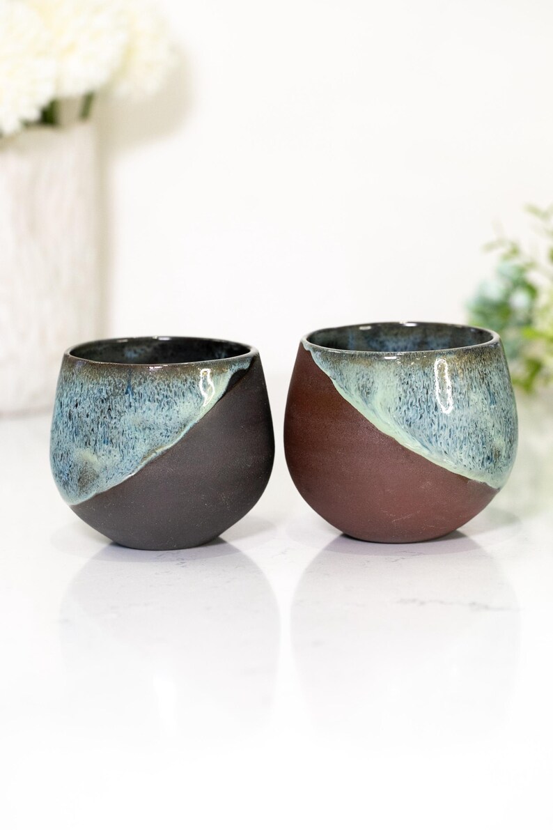 Pu&ograve; includere: Due bicchieri da vino senza stelo in ceramica fatti a mano. Uno &egrave; marrone scuro e blu, l'altro &egrave; marrone e blu. La met&agrave; superiore di ogni bicchiere &egrave; blu screziato, mentre la met&agrave; inferiore &egrave; marrone pieno.