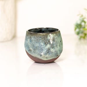 Pu&ograve; includere: Un bicchiere in ceramica fatto a mano con una forma organica unica. L'esterno presenta una miscela di smalto blu e verde su una base marrone scuro. L'interno &egrave; blu scuro. Ideale per le bevande.