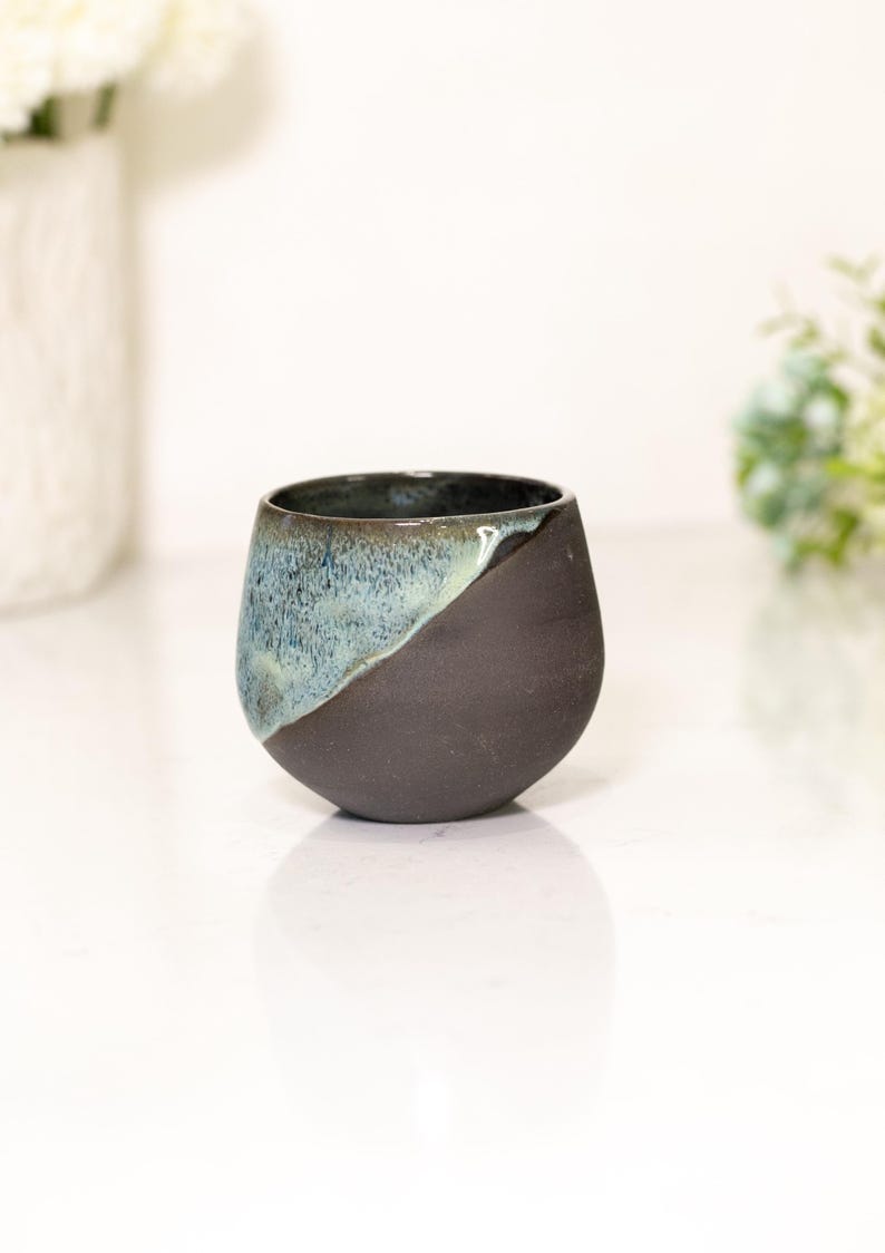 Pu&ograve; includere: Una tazza in ceramica fatta a mano con un design unico. La tazza &egrave; di colore marrone scuro nella met&agrave; inferiore e passa a una glassa blu-verde nella met&agrave; superiore. Ha una forma arrotondata e una finitura liscia.