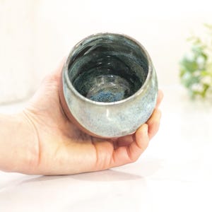Pu&ograve; includere: Una ciotola in ceramica fatta a mano con una smaltatura unica. La ciotola, tenuta in mano, presenta una miscela di colori blu, verde e grigio. L'interno ha un aspetto pi&ugrave; scuro e strutturato, mentre l'esterno &egrave; liscio e lucido. Perfetta per servire o esporre.