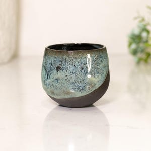 Pu&ograve; includere: Una ciotola in ceramica fatta a mano con un design unico. La ciotola presenta una base nera opaca scura che si trasforma in una glassa screziata blu e turchese. L'interno &egrave; di colore scuro e lucido.