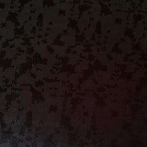 May include: A dark, textured fabric with a pattern of irregular, abstract shapes in varying shades of black. The design creates a subtle, mottled effect across the surface, suitable for apparel or home decor.