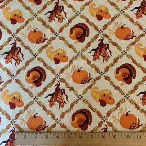 May include: Thanksgiving-themed fabric featuring a repeating pattern of pumpkins, cornucopias, turkeys, and corn. The design is set against a cream-colored background with a diamond grid of leaves and acorns. The fabric is measured with a ruler.