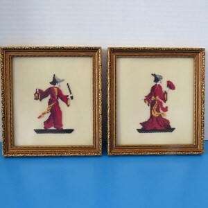 Peut inclure: Deux œuvres d'art encadrées en point de croix. Chacune représente une figure en robe rouge, l'une tenant une lanterne et une épée, l'autre un éventail. Les figures sont sur une base noire, sur fond crème, dans des cadres dorés ornés.