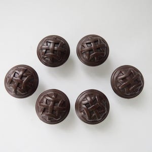 May include: Six dark brown, round buttons with a woven basket design. The buttons are arranged in a circular pattern against a white background. These buttons are suitable for sewing and craft projects.