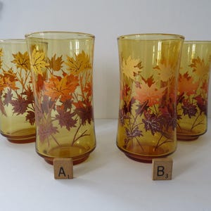 May include: Four amber-tinted drinking glasses, each decorated with a fall leaf pattern. The leaves are in shades of yellow, orange, and burgundy. The glasses are cylindrical with a flared base.
