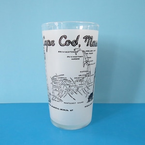 Peut inclure: Un grand verre transparent avec une finition blanche givrée. Le verre présente une carte noire de Cape Cod, Massachusetts, avec les noms des villes et les points de repère. Les mots "Cape Cod, Mass" sont imprimés en haut. Le verre est posé sur un fond bleu clair.