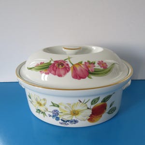 May include: White ceramic casserole dish with a lid. The dish features a floral design with pink, yellow, and green flowers. The lid has a gold trim.