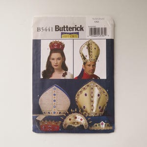 May include: A Butterick B5441 Making History sewing pattern envelope featuring illustrations of various headpieces including a red crown, a tall gold mitre, and a textured beige mitre, all decorated with colorful faux gemstones and trim.