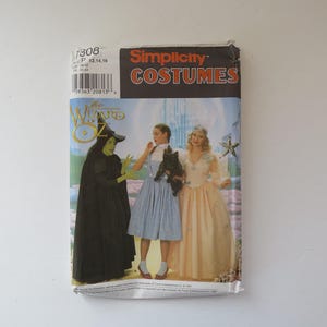May include: A Simplicity Costumes sewing pattern envelope for The Wizard of Oz, featuring illustrations of the Wicked Witch in a black dress, Dorothy in a blue gingham dress with a dog, and Glinda in a peach gown, with pattern number 7308 and size P 12,14,16.