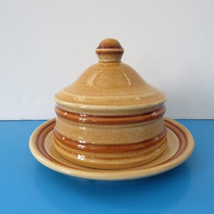 Peut inclure: Un beurrier en céramique avec un couvercle et une assiette assortie. Le beurrier est brun et beige avec des rayures brunes.