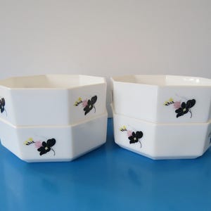 May include: Set of four white ceramic bowls with a hexagonal shape. Each bowl features a black and pink floral design.