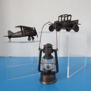 May include: A vintage-style collection featuring a metal lantern with a clear glass globe, a biplane, and a classic car. The objects are displayed on clear acrylic stands against a blue background, evoking a sense of nostalgia.
