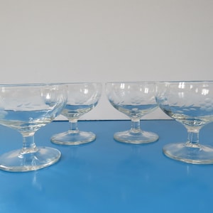 Peut inclure: Quatre coupelles à dessert en verre transparent avec des motifs gravés sur les bols et les tiges. Les coupelles sont sur une surface bleue.