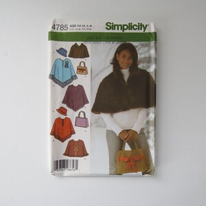 Peut inclure: Un paquet de patrons de couture Simplicity, montrant une femme portant une cape en fausse fourrure et un sac à main. Le paquet comprend des illustrations de capes, de chapeaux et de sacs à main. Le texte "Simplicity" est visible.