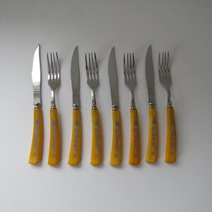 May include: Set of eight yellow-handled cutlery, including knives and forks. The handles feature a blue floral design.