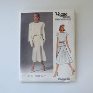 Peut inclure: Une pochette de patron de couture Vogue Patterns American Designer par John Anthony, numéro 1387. Le devant présente une photographie et une illustration d'un ensemble deux pièces composé d'un haut clair et d'une jupe assortie avec une veste.