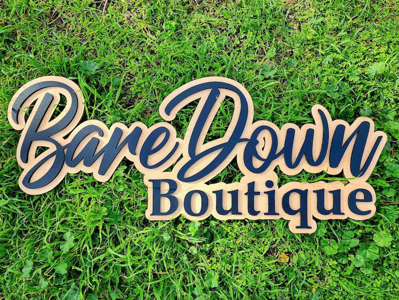 May include: A wooden sign with the text "Bare Down Boutique" in black lettering on a brown background.