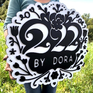 May include: Black and white wooden sign with the number 222 and the text "BY DORA" surrounded by floral designs.
