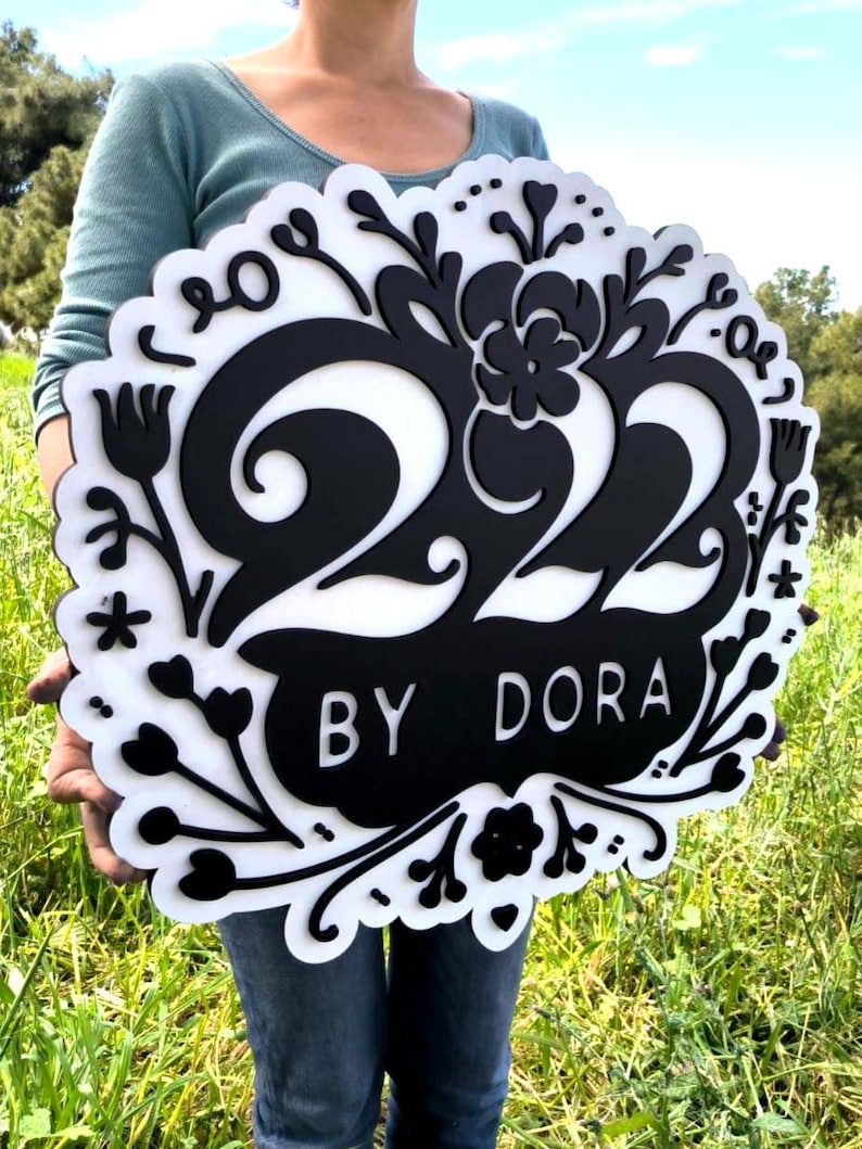 May include: Black and white wooden sign with the number 222 and the text "BY DORA" surrounded by floral designs.