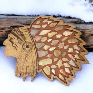 Puede incluir: Arte de pared de madera con un tocado nativo americano con un diseño de puntas de flecha. El tocado es marrón y tiene un fondo rojo. Las puntas de flecha son de piedra y tienen varias formas y tamaños.