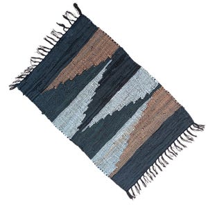 Könnte beinhalten: Ein rechteckiger Teppich mit gewebtem Design. Der Teppich hat diagonale Streifen in Schwarz-, Braun- und Grautönen. Die Kanten sind mit Fransen versehen. Dieser Teppich eignet sich für ein Wohn- oder Schlafzimmer.