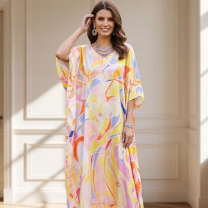 May include: A long, flowing caftan dress with a vibrant, abstract pattern in shades of yellow, orange, pink, and blue. The dress has wide sleeves and a V-neckline. The model is wearing silver heels and jewelry.
