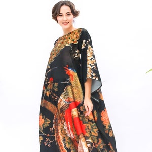 May include: A black, floor-length kaftan with a vibrant bird and floral print. The design features a large pheasant with red, orange, and gold plumage, set against a backdrop of branches and flowers. The kaftan has wide sleeves and a relaxed fit.