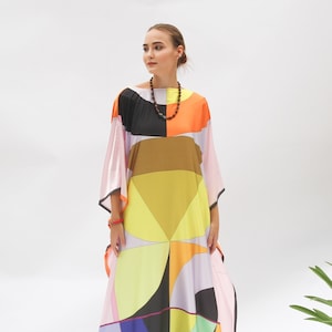 Puede incluir: Un vestido maxi largo y fluido con un patrón geométrico en tonos naranja, amarillo, azul, verde, rosa y negro. El vestido tiene un corte holgado y cómodo y un escote amplio.