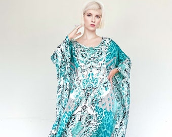 Op de afbeelding: Een zwierige, turquoise en wit patroon caftan jurk. De jurk heeft een uniek ontwerp met abstracte en dierenprint elementen. Het model draagt zwarte plateau hakken. De jurk heeft wijde mouwen en een relaxte pasvorm.